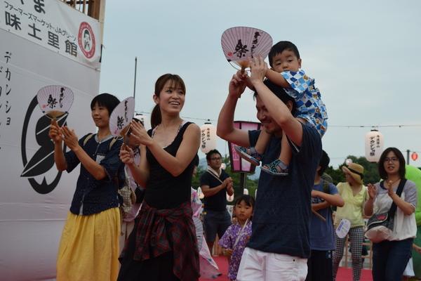 甚平姿の子供を肩車している父親と母親らがうちわを手に持って楽しそうに踊っている写真