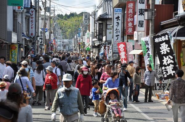 店前に旗が並び、沢山の人でにぎわう街並みの写真