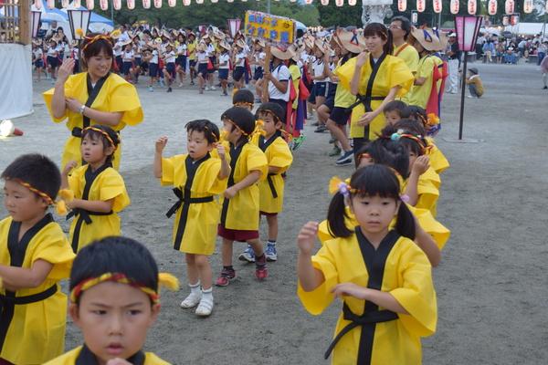 ねじり鉢巻きに黄色い法被姿の子供らが先生と一緒に真剣な表情で踊っている写真