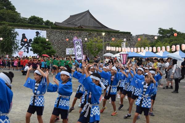 鉢巻きに青い法被姿の子供たちが両手を挙げて踊っている写真
