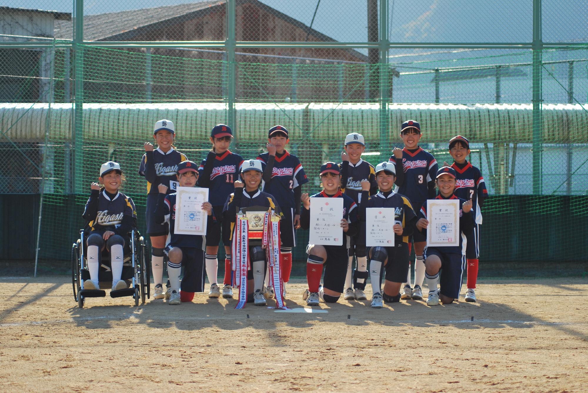 ソフトボールの試合で準優勝した盾や表彰状を持って部員たちが記念撮影している