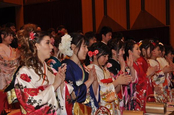 客席の振袖を着た新成人達が手拍子を打って歌を歌っている様子の写真