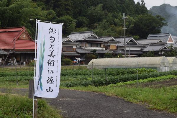 畑の道沿いに「俳句×美術in篠山」と書かれた上り旗が飾られている写真