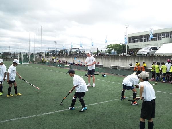 白いティシャッを着た子供達が先の曲がった棒でボールを誘導している写真