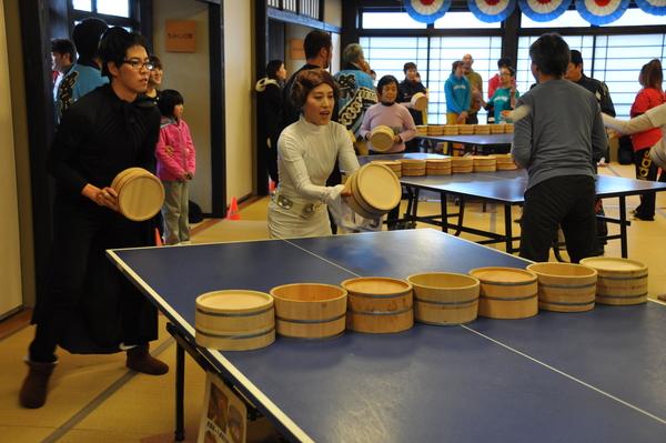 全身白の服装の女性と、全身黒の服装の男性がペアで桶を持って卓球をしている写真