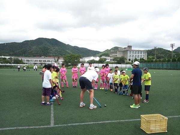 芝生の上でそれぞれのユニフォームを着た子供達が、ルーク選手から指導を受けている写真
