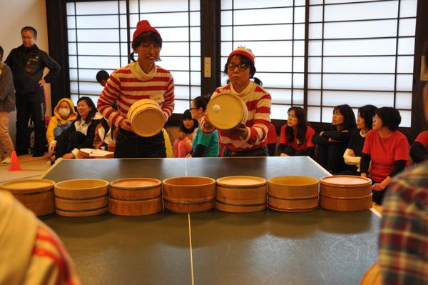 お揃いの赤と白のボーダーの服装をした女性2人の参加者が桶で卓球をしている写真