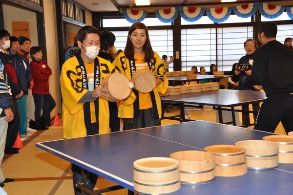 黄色の法被を着た男女ペアの参加者が桶を持って卓球をしている写真