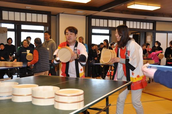 白い法被を着た男性と女性のペアが桶を持って卓球をしている写真