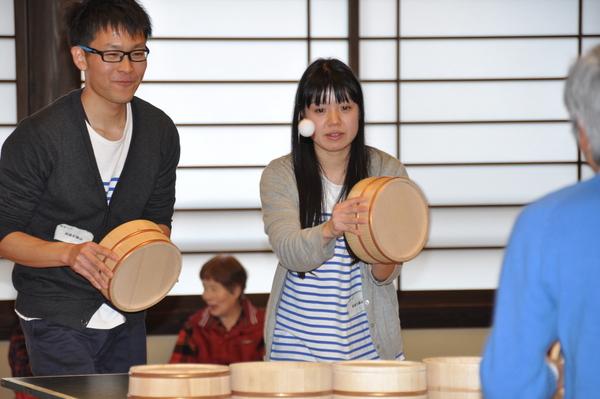 お揃いの青と白のボーダーのTシャツを着た男女ペアの参加者が桶を持って卓球をしている写真
