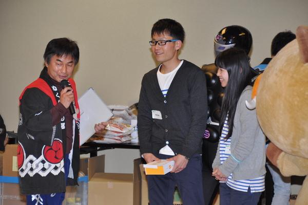 マイクを持った男性が話をしていて、右側にいる男女ペアの参加者が笑っている写真