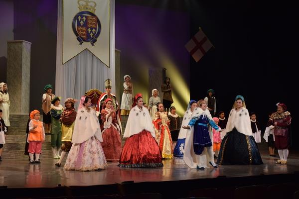 青の衣装で白のマントを着ている王子役が両手を広げているのを周りの出演者がみている舞台の写真