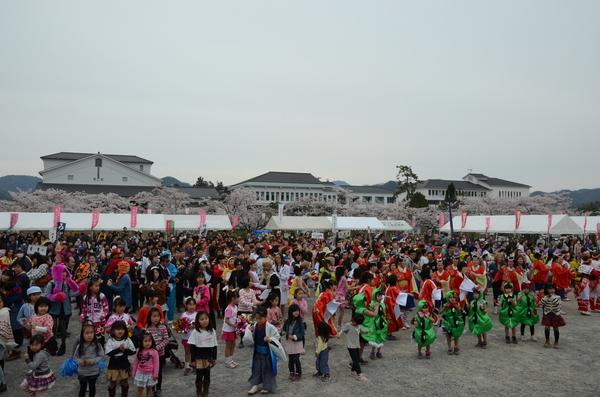 会場の広場で大勢の市民が様々ないでたちをした格好で音楽に合わせて一斉に踊っている写真