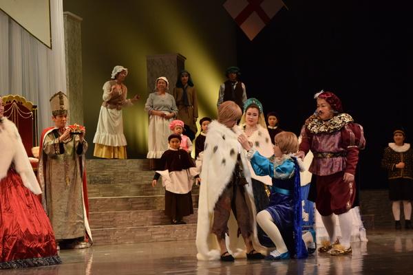 青、紫の衣装を着た子が茶色の衣装を着た子に白いマントを着せている、その様子を見ている出演者の写真