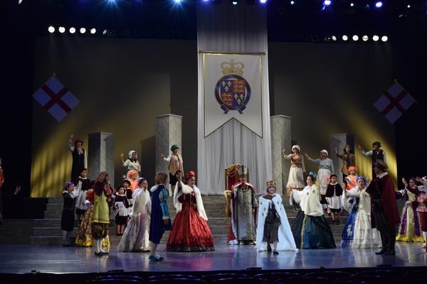 様々な衣装を着た出演者が、王冠を被り白のマントを着た方主人公の方を向き、右手をあげたり、笑顔で写っている写真