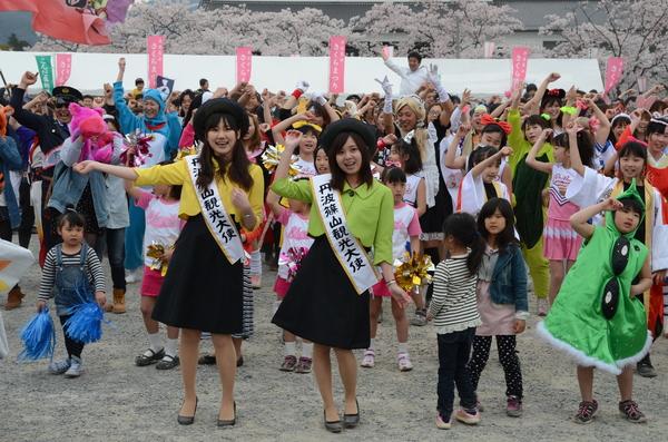 黒色のベレー帽にスカート、黄色と色違いの緑色のジャケットを着た丹波篠山観光大使の女性の二人が市民と一緒に総踊りに参加している写真