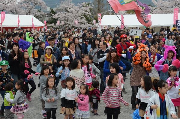 桜並木のテントの前で老若男女沢山の市民が総踊りに参加している写真