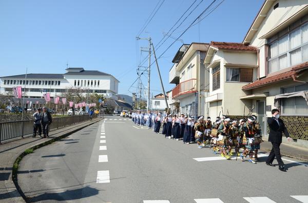 青空の下、祭りの行事に参加した子供や大人たちが長い列を歩いている写真