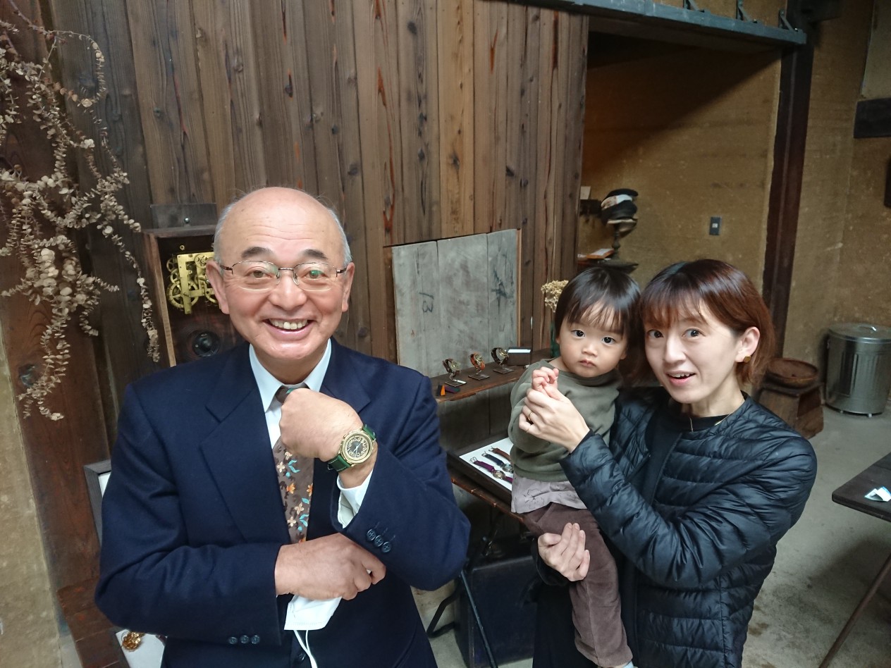 左手つけた腕時計を見せる市長と、こどもを抱いた女性の職人