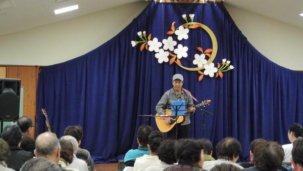「古市地区文化活動発表会」トリを務めた進戸 納さんのギター弾き語り正面の様子と観覧者の写真