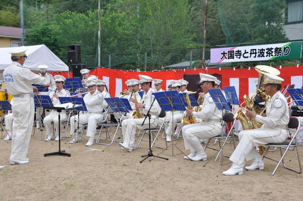 白い帽子と衣装を着た県警音楽隊の方々がサックスやフルートなどの楽器で演奏している写真