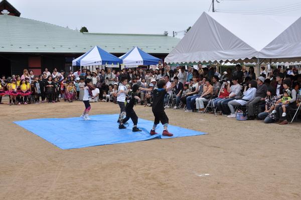 ブルーシートの上でダンスをしている子供達とその様子を見ている人々の写真
