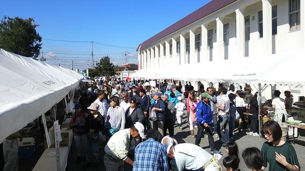 校舎の横に設置されたテントで催しがありその横を歩く人々の写真