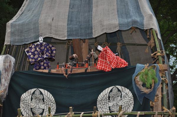 山車の中で紫色と橙色着物を着た操り人形の劇が始まっている写真