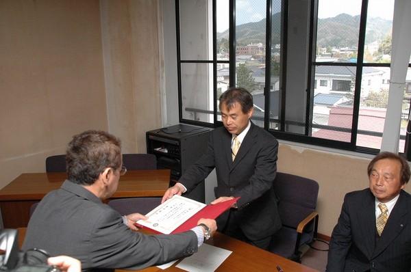 こばたけ 政行議員が、グレーのスーツを着ている男性より証書を手渡しでもらっている様子の写真