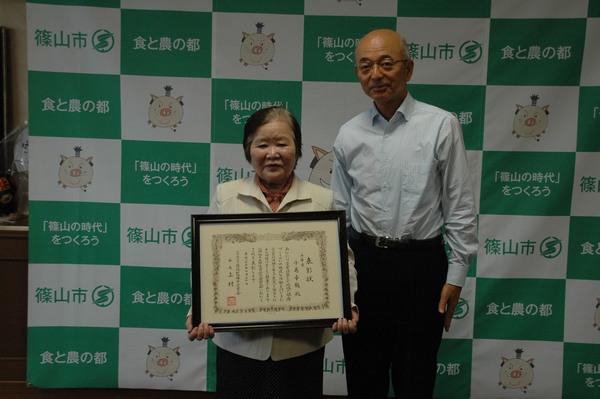 「恩賜財団母子愛育会会長表彰」授与され表彰状を両手に持った小島さんと市長の記念写真