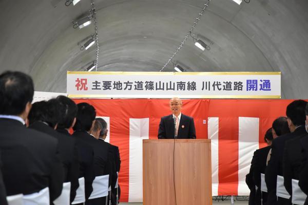 紅白の幕の前で市長が参加者達へ話をしている写真