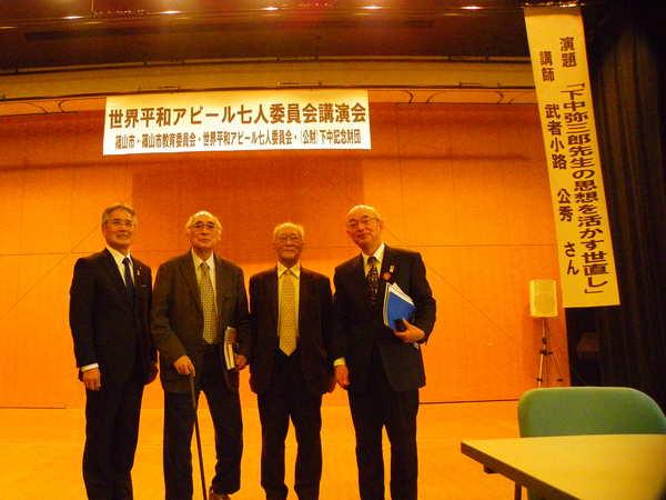広いホールの公演会場で関係者の男性、武者小路さん、小沼さん、関係者の男性、市長との記念写真