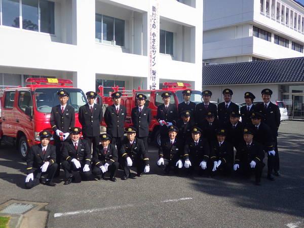 引渡された消防車2台の前で消防団員が記念撮影している写真
