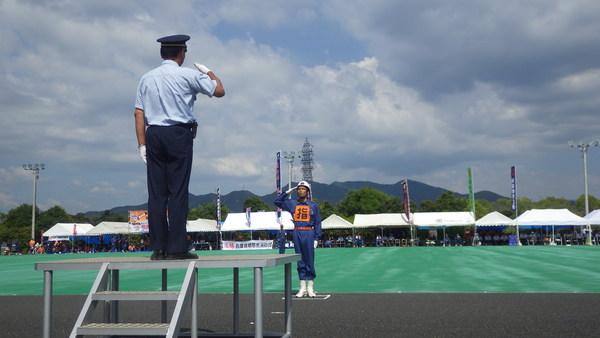 消防団員が敬礼台に上がっている男性に向かって敬礼をしている様子の写真