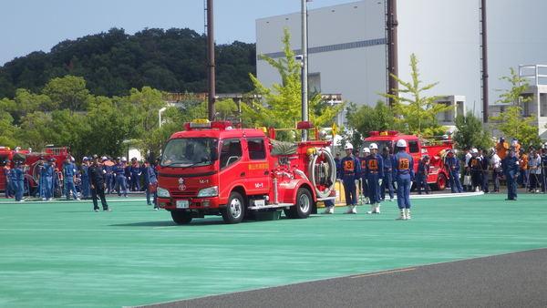 消防者が中央にあり、消防団員が所定の位置について消防訓練を行おうとしている様子の写真