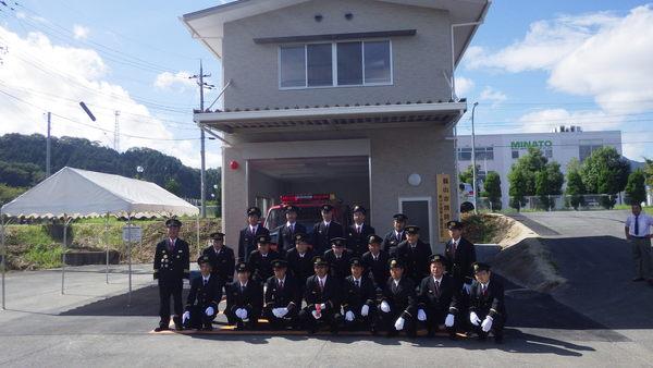 消防詰所の前で制服姿の消防団員らが記念撮影している写真