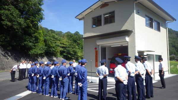 新しく完成した消防団詰所前で制服を着た消防団員が整列している写真
