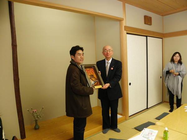 額に入った太陽と壺の絵が描かれている作品を黄 肇崇(こう ちょうすう)さんと市長が視察参加者にも見えるように、手に持っている写真