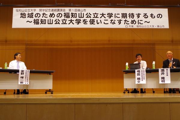 福知山公立大学副学長の富野暉一郎さん、九州大学の嶋田さん、市長が座り、市長がマイクを持ち講演している写真