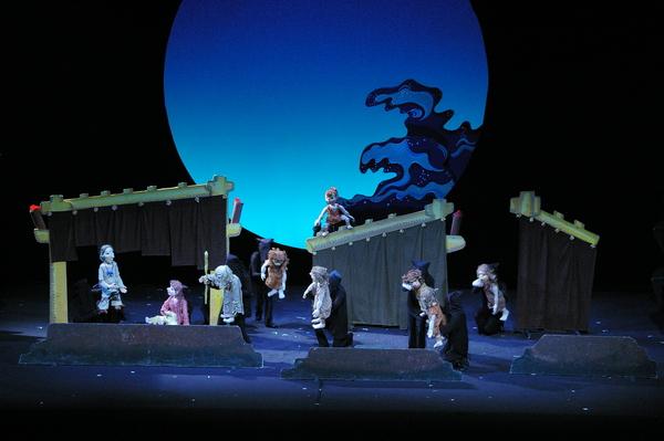 舞台の上で沢山の登場人物の人形と人形を操っている黒子が「火の鳥」の話を演じている様子の公演の一場面の写真