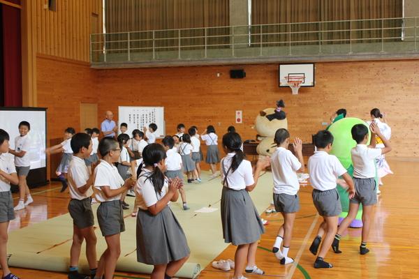 マスコット人形と一緒に子供達が輪になりデカンショ踊りを踊っている写真