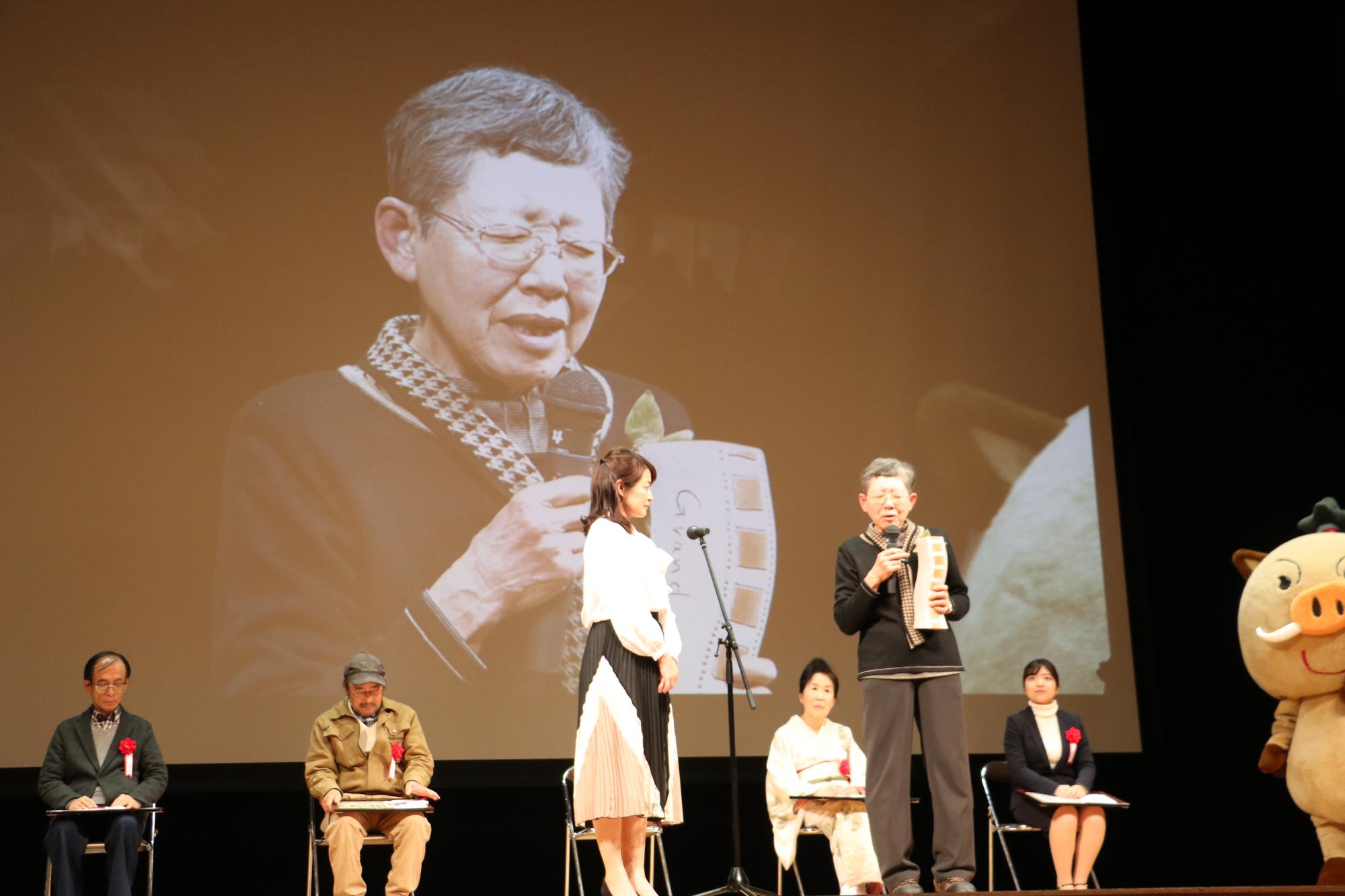 大賞の阪下さんがマイクを持って話されている姿がスクリーンに大きく映し出され、その話をきく熊谷奈美さんと他の受賞者の方々の写真