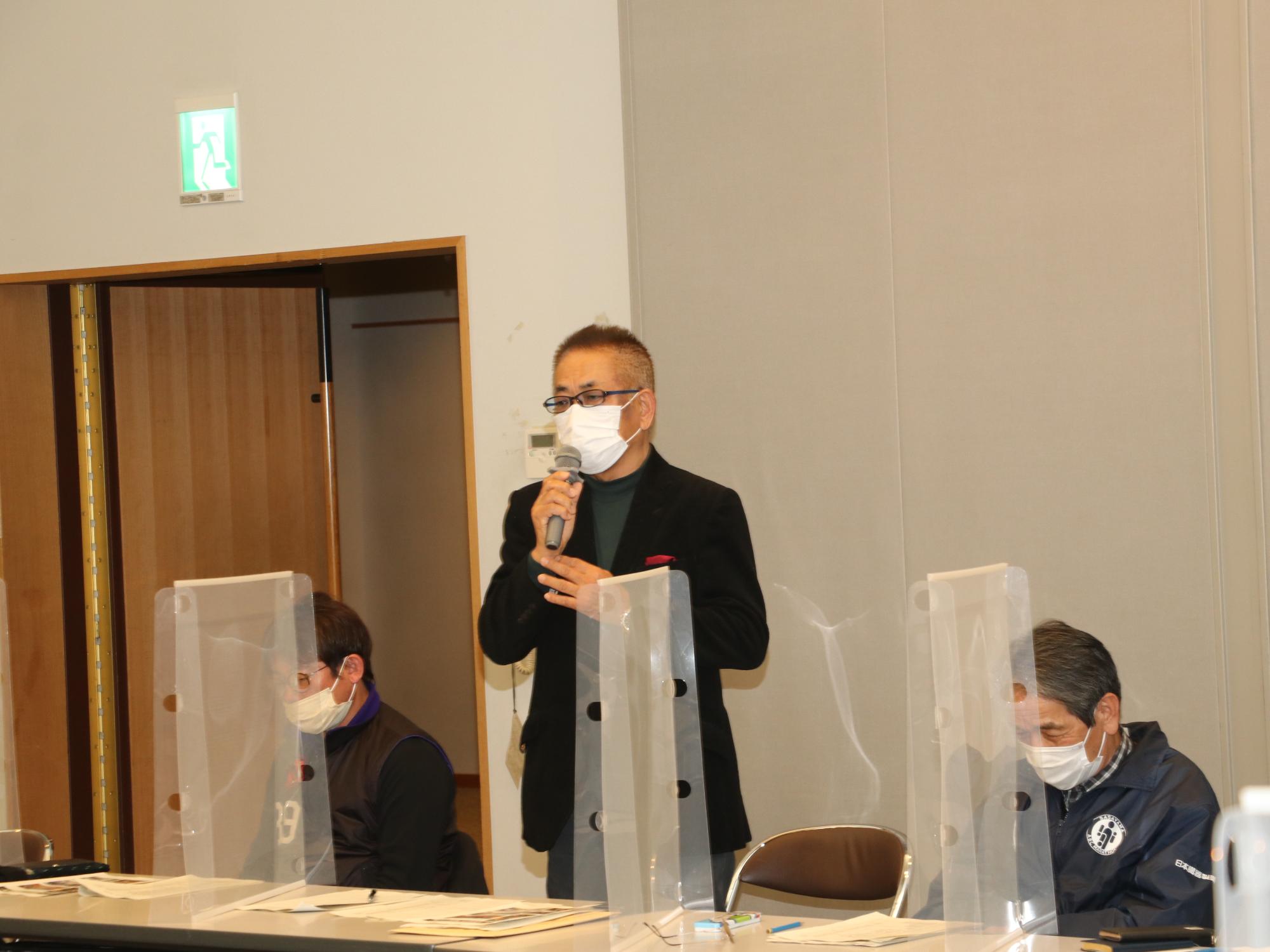 会長が立ってマイクを持って話されている