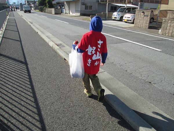 「ささ山が好き」のバックプリントされた赤いTシャツを着ている小学生ぐらいの子どもがゴミ袋を持っている後姿の写真