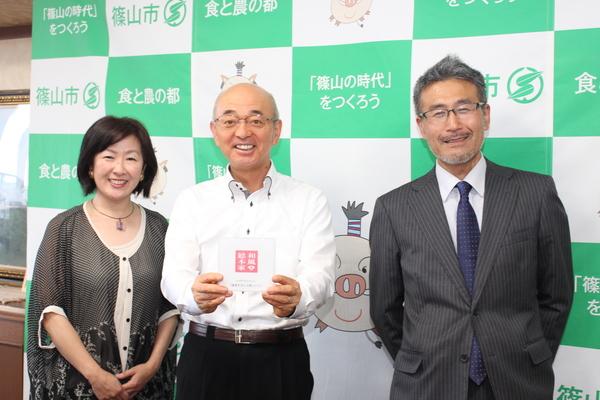 青山 佳司さんと久保 佳代さんの間に酒井 隆明市長が「和風総本家」のビデオを持っている写真