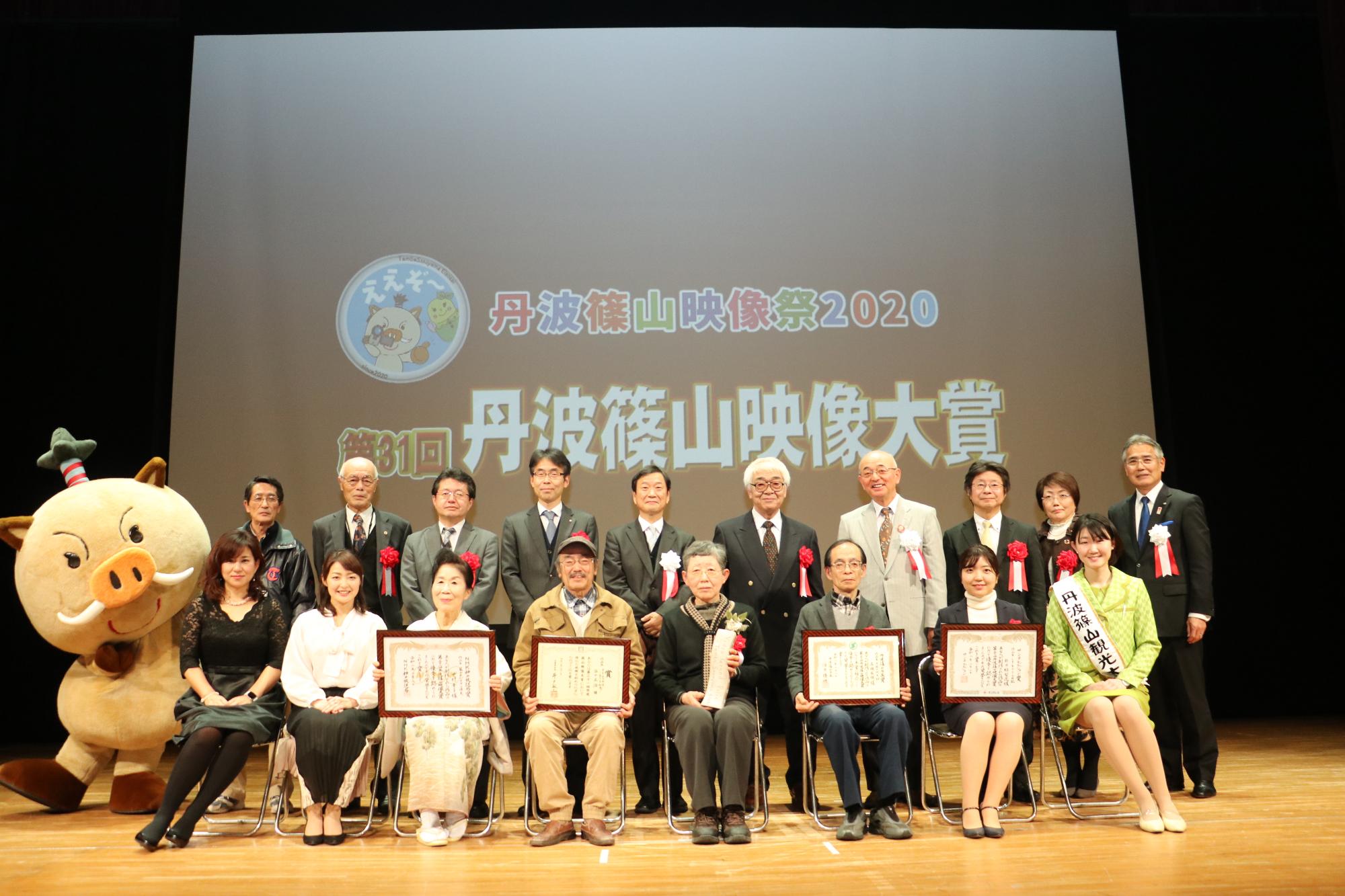 舞台で記念撮影をする受賞者の方々や、観光大使、まるいのなどの写真
