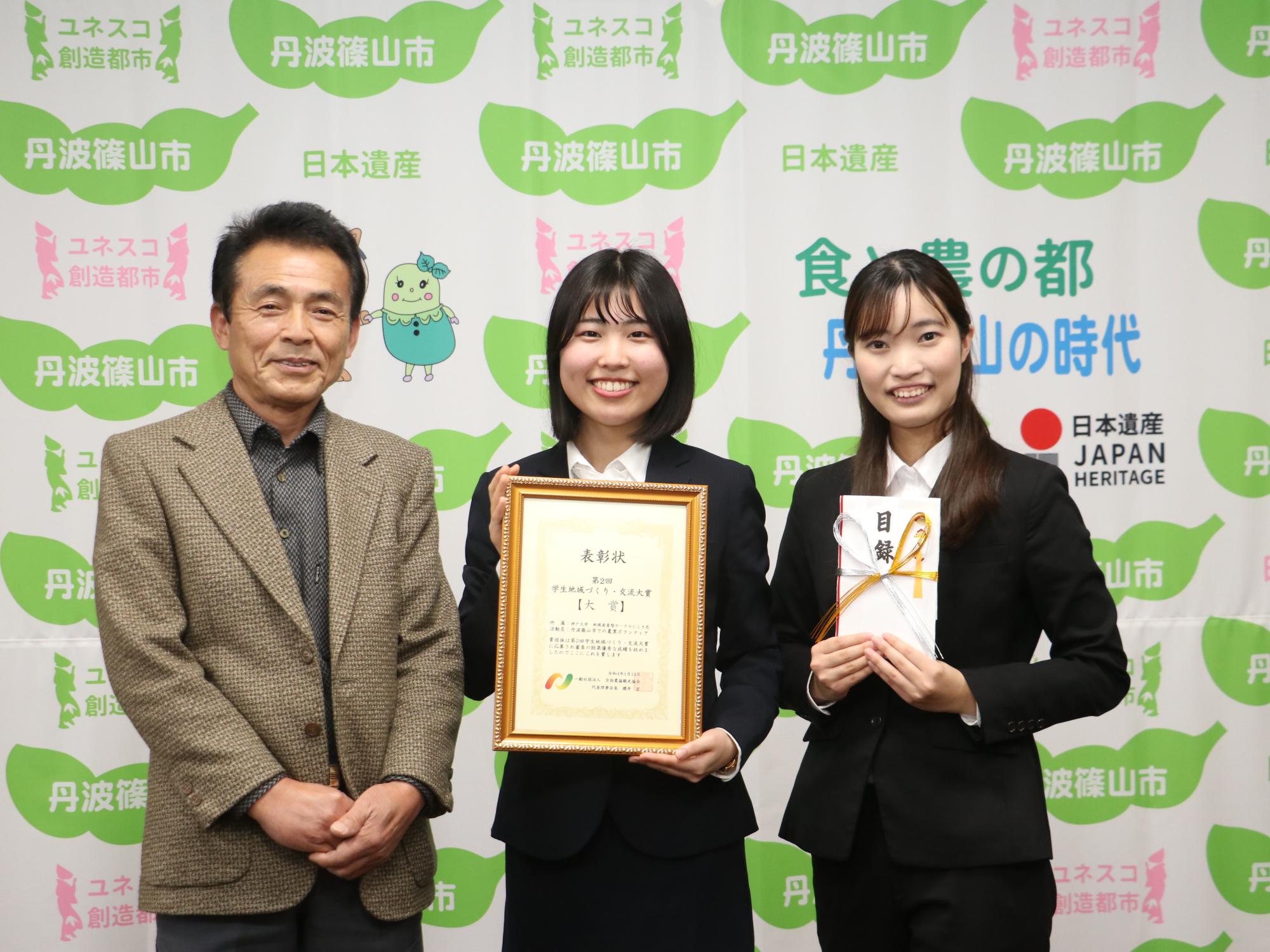 真ん中の女性が表彰状を手に持ち、右隣の女性が目録を手に持ち、左隣に会長が立っている