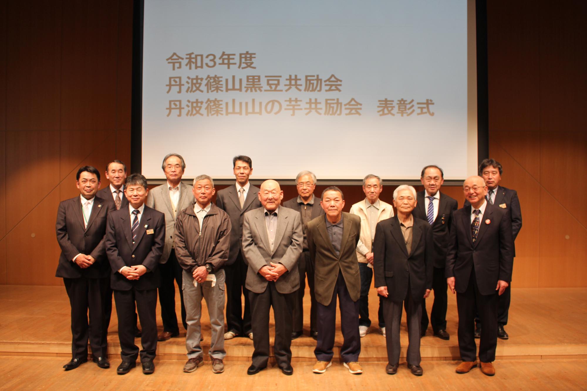 舞台の上で、受賞者が2列に並んで立っている