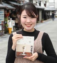 商店街を背景に、ことりっぷ丹波篠山を手に持った女性が立っている