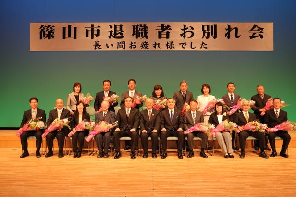 花束を受け取った退職者達が市長ら関係者と記念写真を撮っている写真